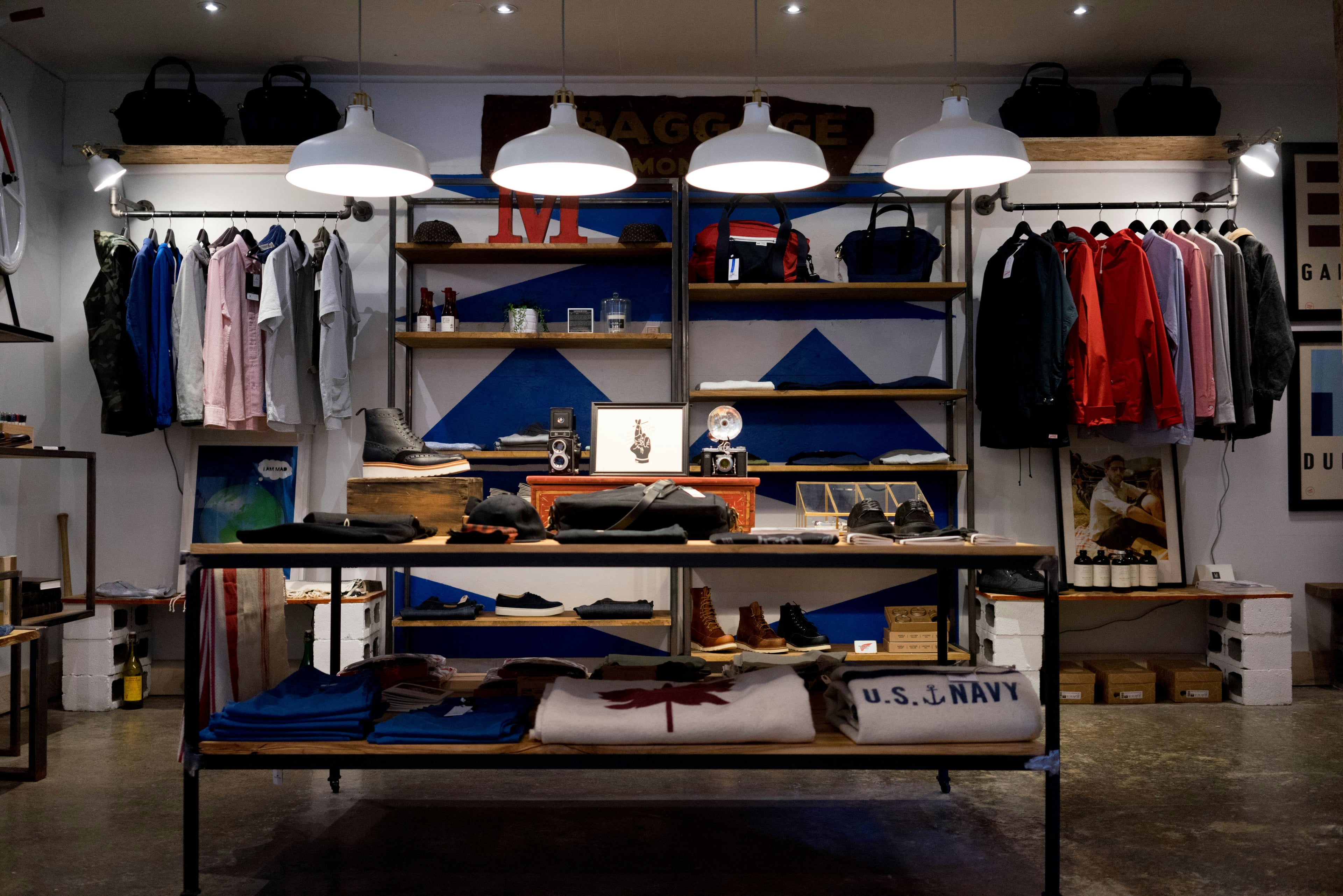 Interior of a small menswear shop, clothing rails along the walls and a display table of folded goods