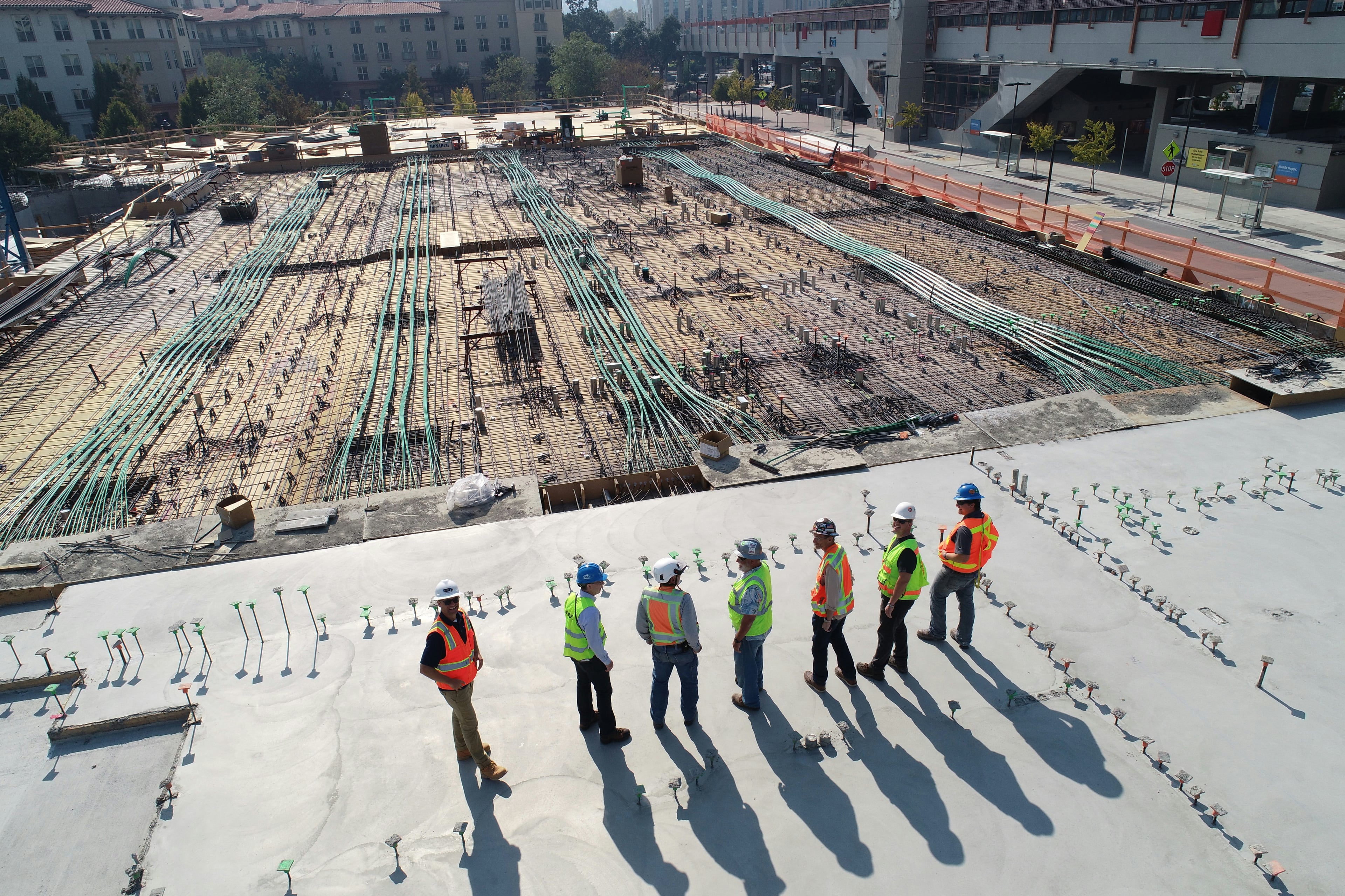 Overhead view of a construction site at golden hour, a line of workers in high-visibility vests casting long shadows